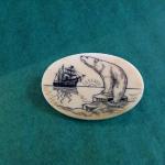 Scrimshaw pin featuring a polar bear and sailing ship. Signed "Nuguruk" on the back.